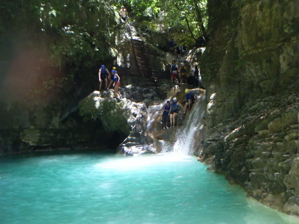 Visitantes bajando por una cascada hacia una poza turquesa entre paredes de roca en Damajagua