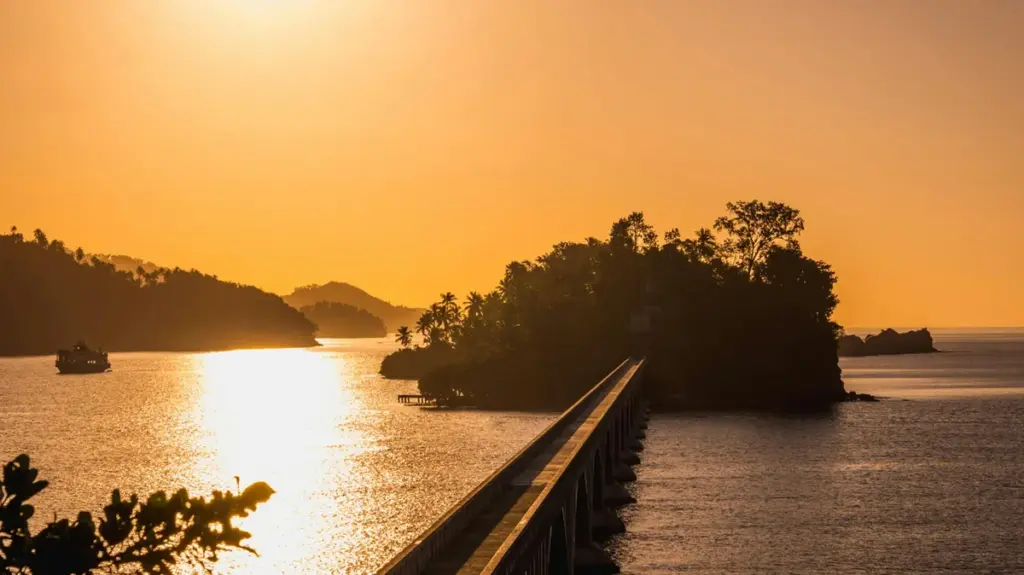 Puente peatonal hacia un cayo de Samaná al atardecer con el sol reflejado en el agua