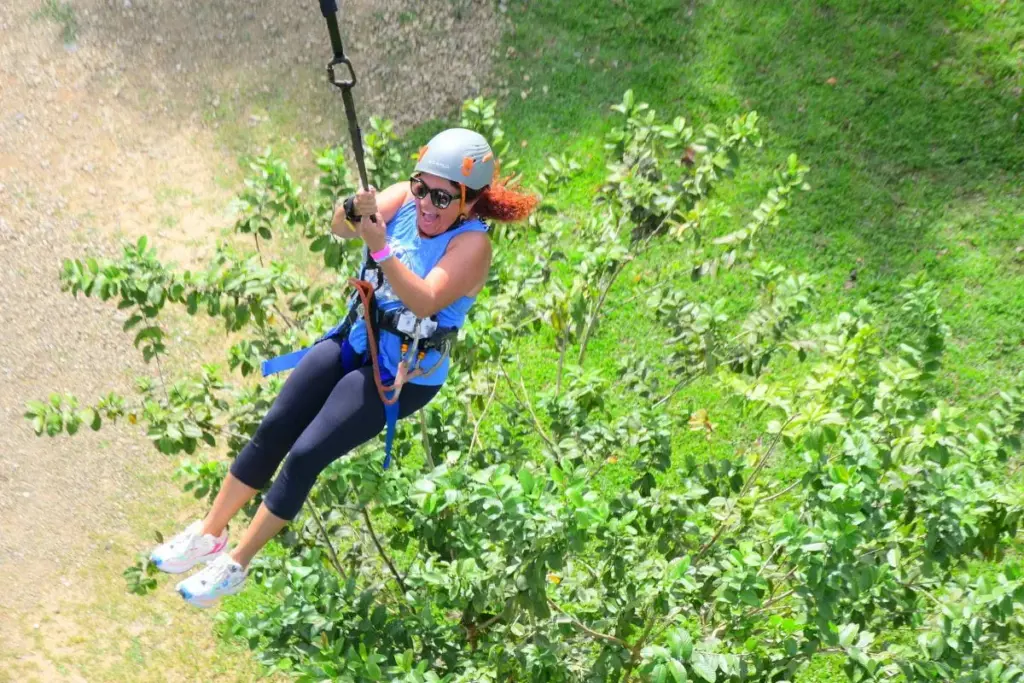 Mujer con casco deslizándose en una tirolesa entre la vegetación