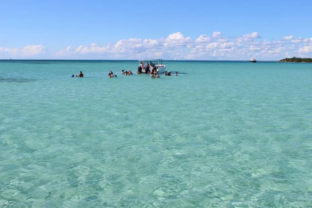 Piscina natural de agua turquesa y poco profunda cerca de Isla Saona con embarcaciones al fondo