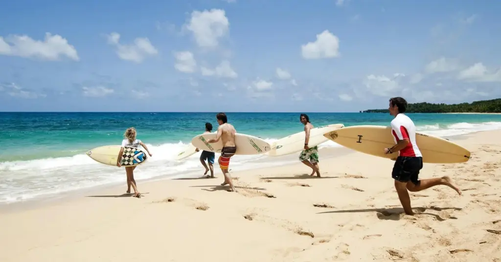 Grupo de surfistas corriendo con sus tablas por la orilla de una playa